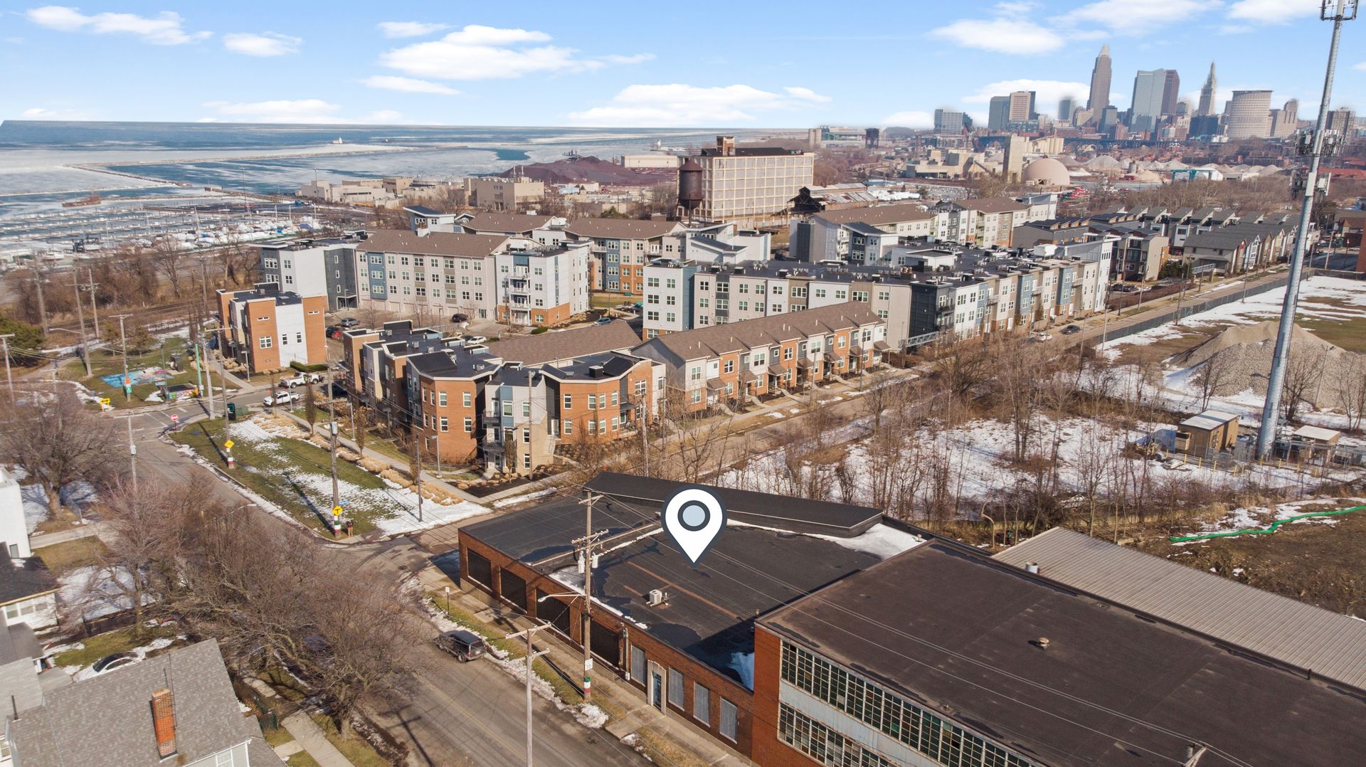 Aerial view of a snow-dusted urban neighborhood with modern residential buildings and a large city skyline in the background.