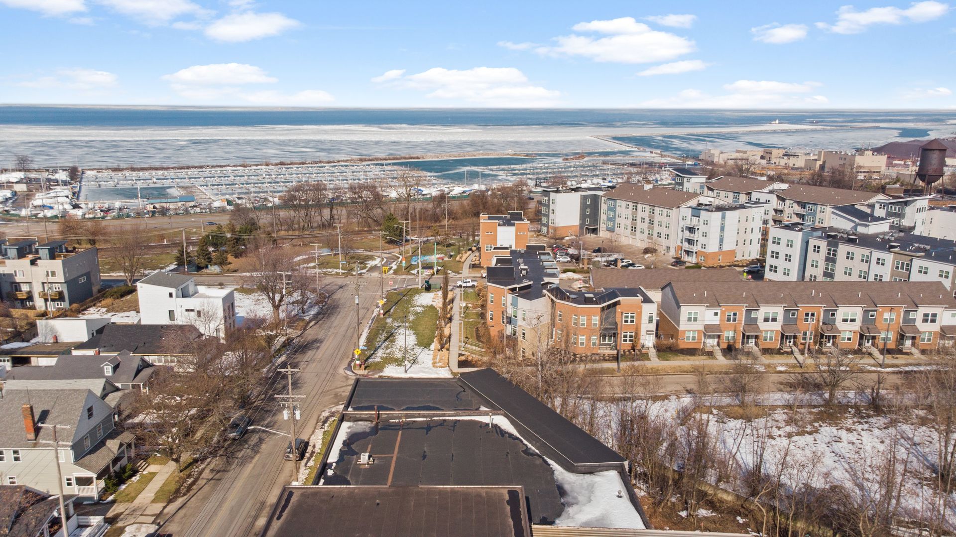 Aerial view of a residential neighborhood with townhouses near a waterfront marina on a partly cloudy day.