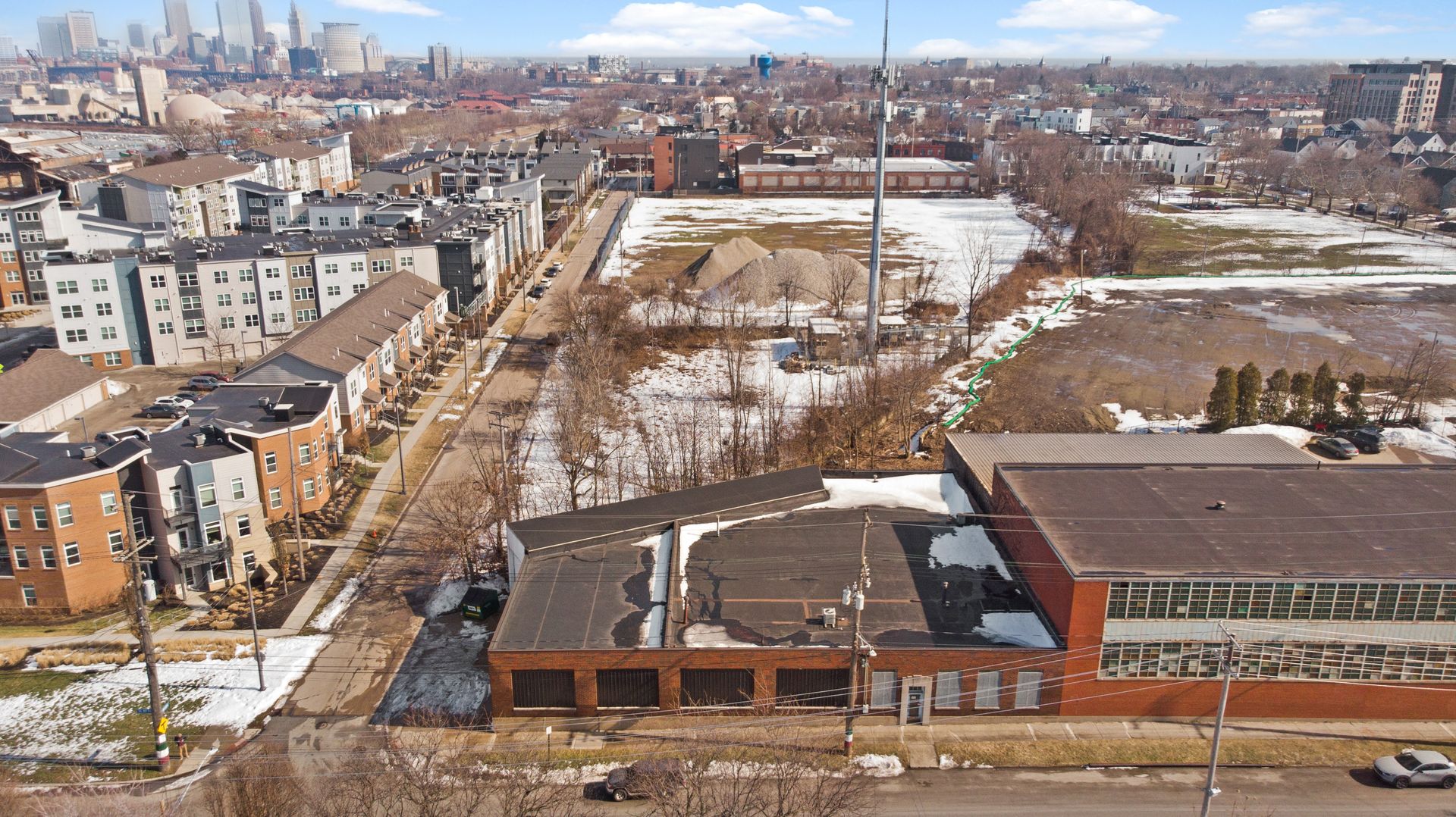 Aerial view of an urban area with residential buildings, empty land, and a city skyline in the background.
