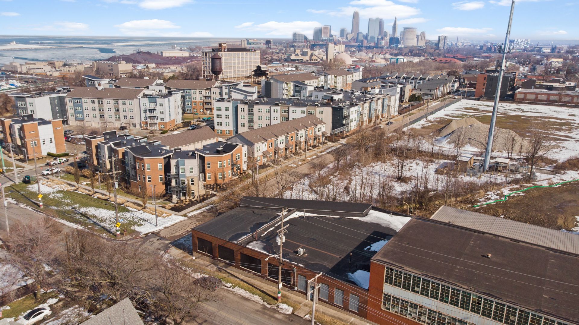 Aerial view of a residential area with modern townhouses and apartments, a snowy landscape, and a city skyline in the background.