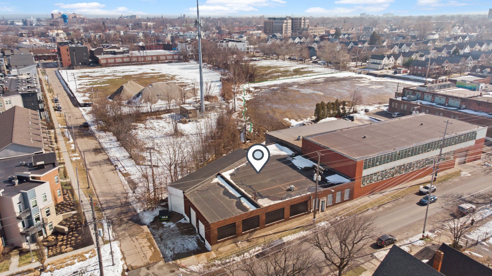 Aerial view of a snowy urban area with residential homes, an industrial building marked with a location pin icon, and a cellphone tower.