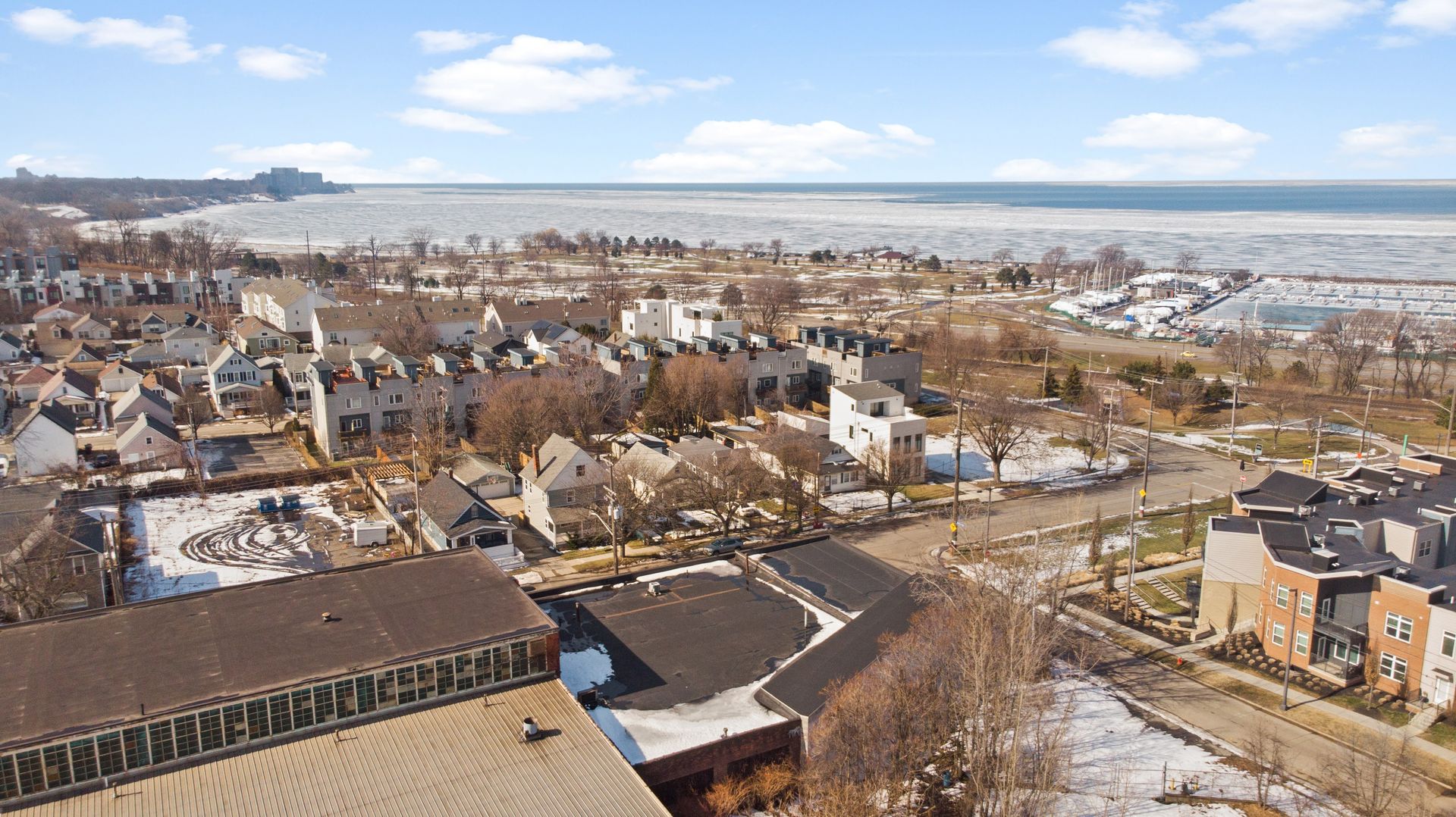 Aerial view of a snowy residential neighborhood near a frozen lake with docks and boats.