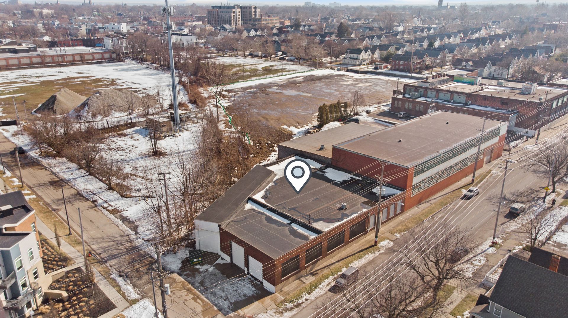Aerial view of an industrial building in a snowy urban area with a location pin icon on the roof.