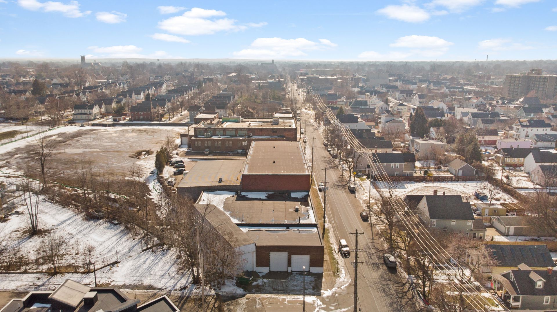 Aerial view of a suburban neighborhood with snow-covered rooftops and roads on a clear day.