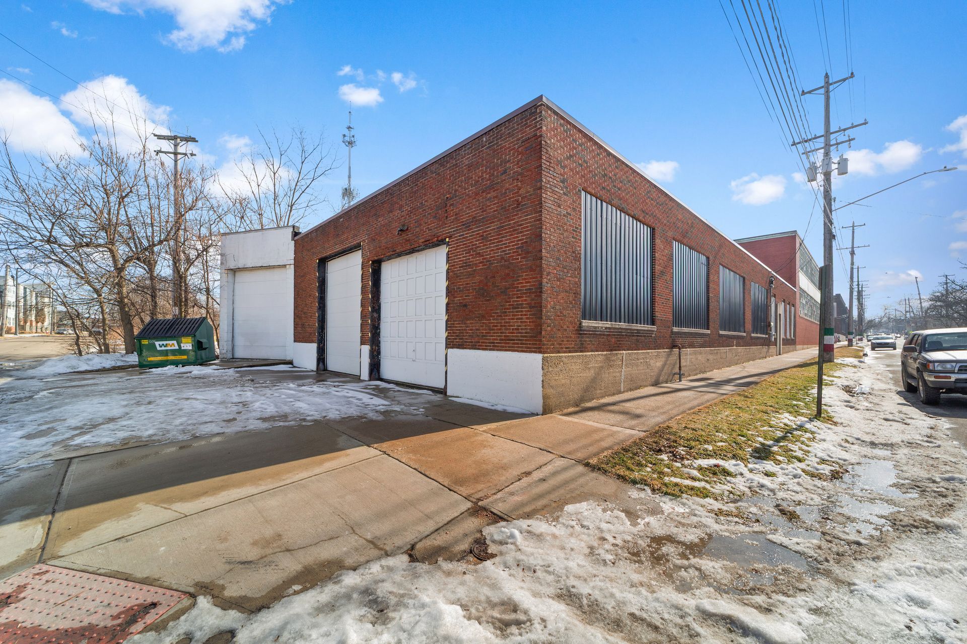 A large brick warehouse building with several garage doors, adjacent to a snow-melted sidewalk and street.
