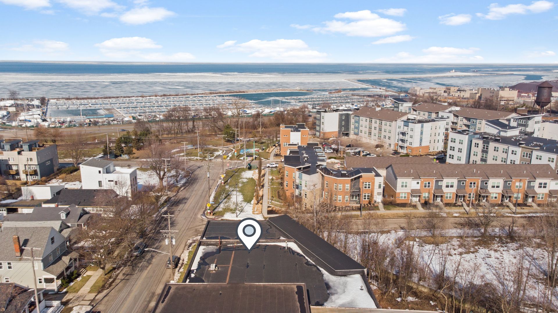 Aerial view of a residential neighborhood near a frozen harbor and lake, with a location pin on a building.