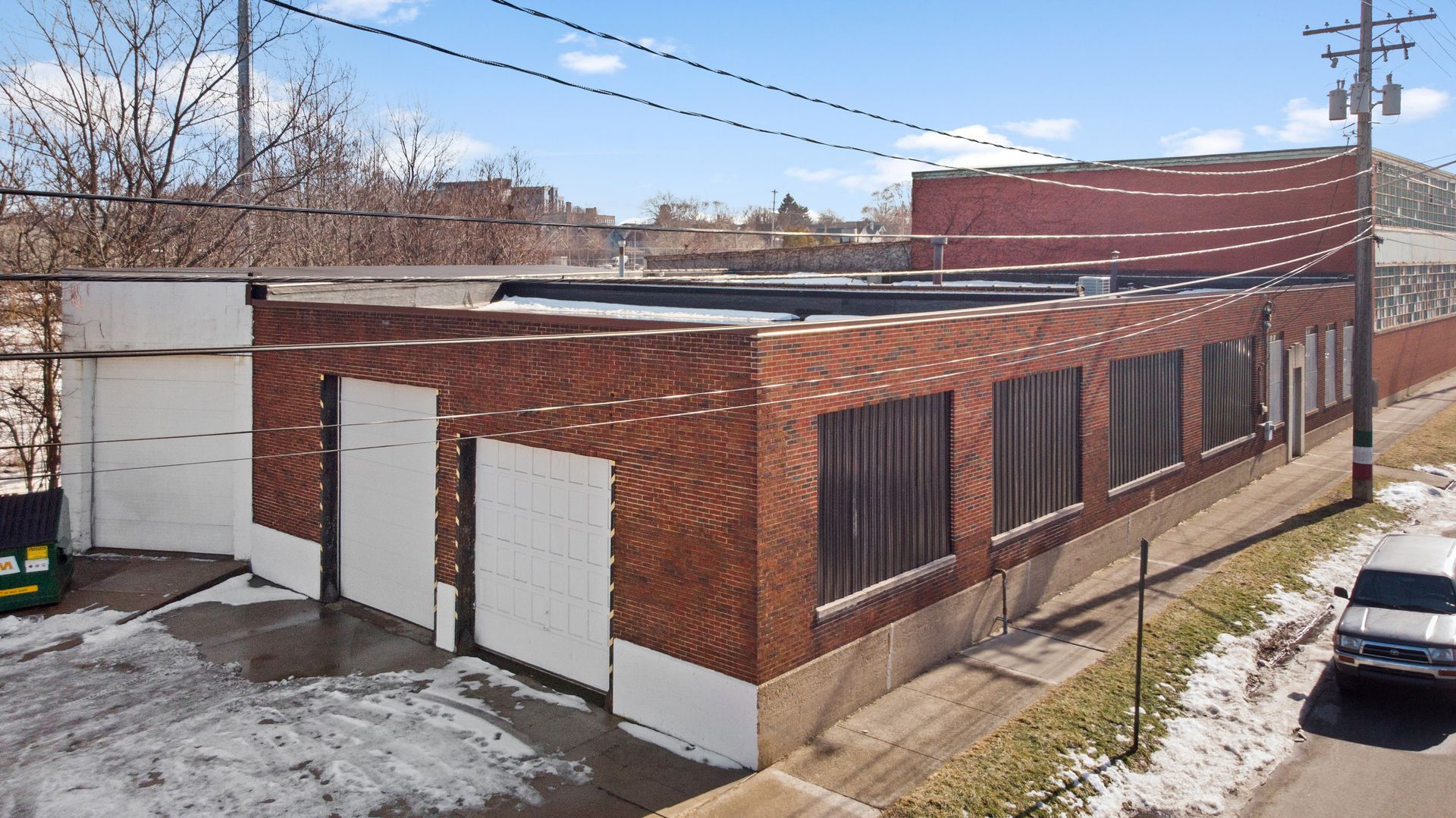 A brick industrial building with two white garage doors, surrounded by snow and utility wires.