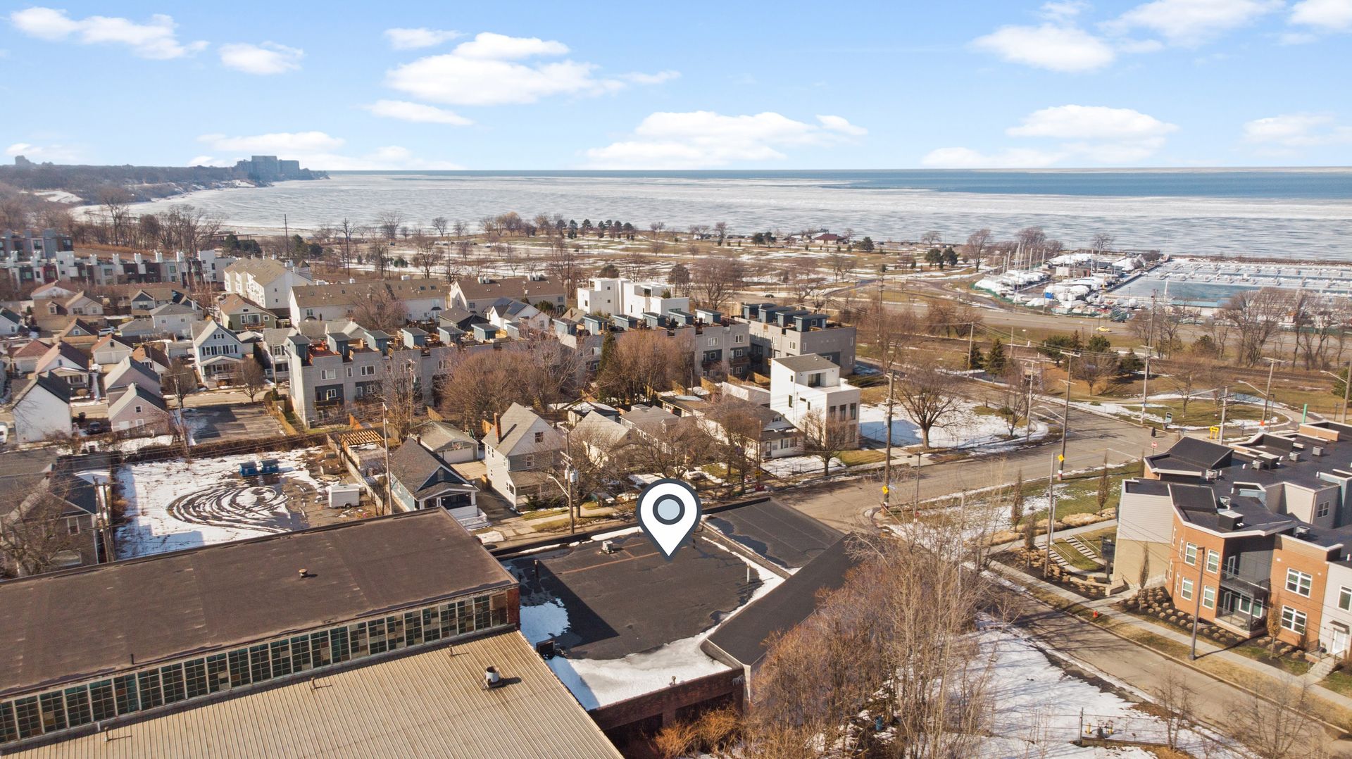 Aerial view of a residential neighborhood near a partially frozen lake, with a location pin icon marking a specific spot.