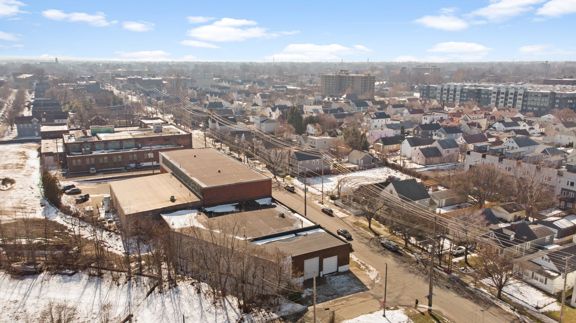 Aerial view of a snowy urban neighborhood with industrial buildings, houses, and streets.