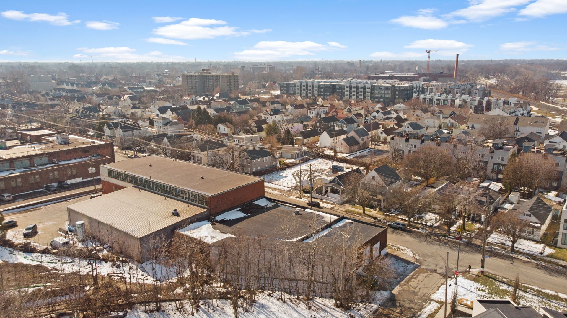 Aerial view of a suburban neighborhood with a mix of residential houses and industrial buildings, partially covered in snow.