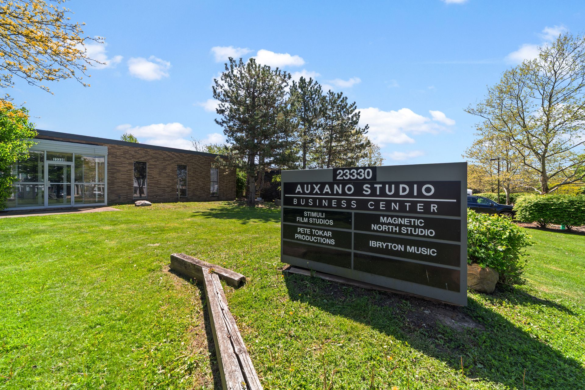 Exterior of Auxano Studio Business Center at 23330, with a lawn, trees, and a tenant sign listing Stimuli Film Studios, Pete Tokar Productions, Magnetic North Studio, and Ibryton Music.